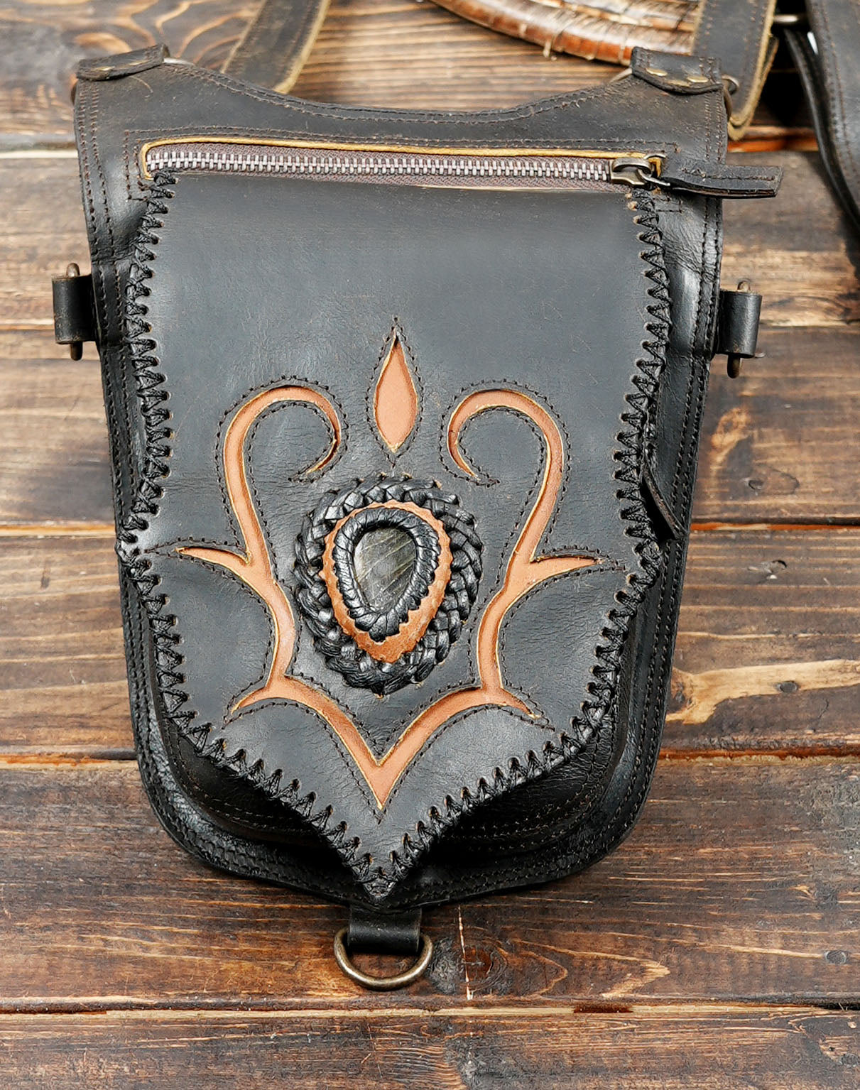 Black leather bag with decorative brown patterns on a wooden surface