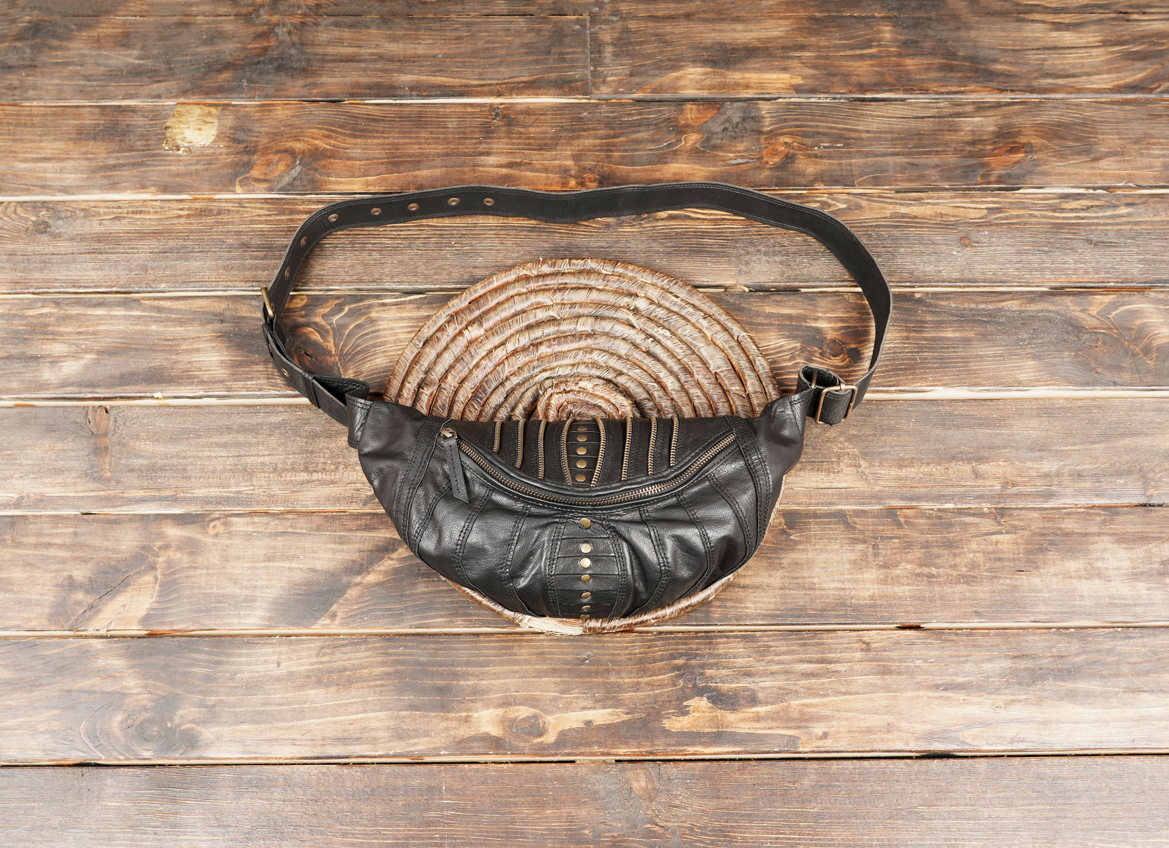 Handmade black leather shoulder belt bag with brass studs and zipper details.
