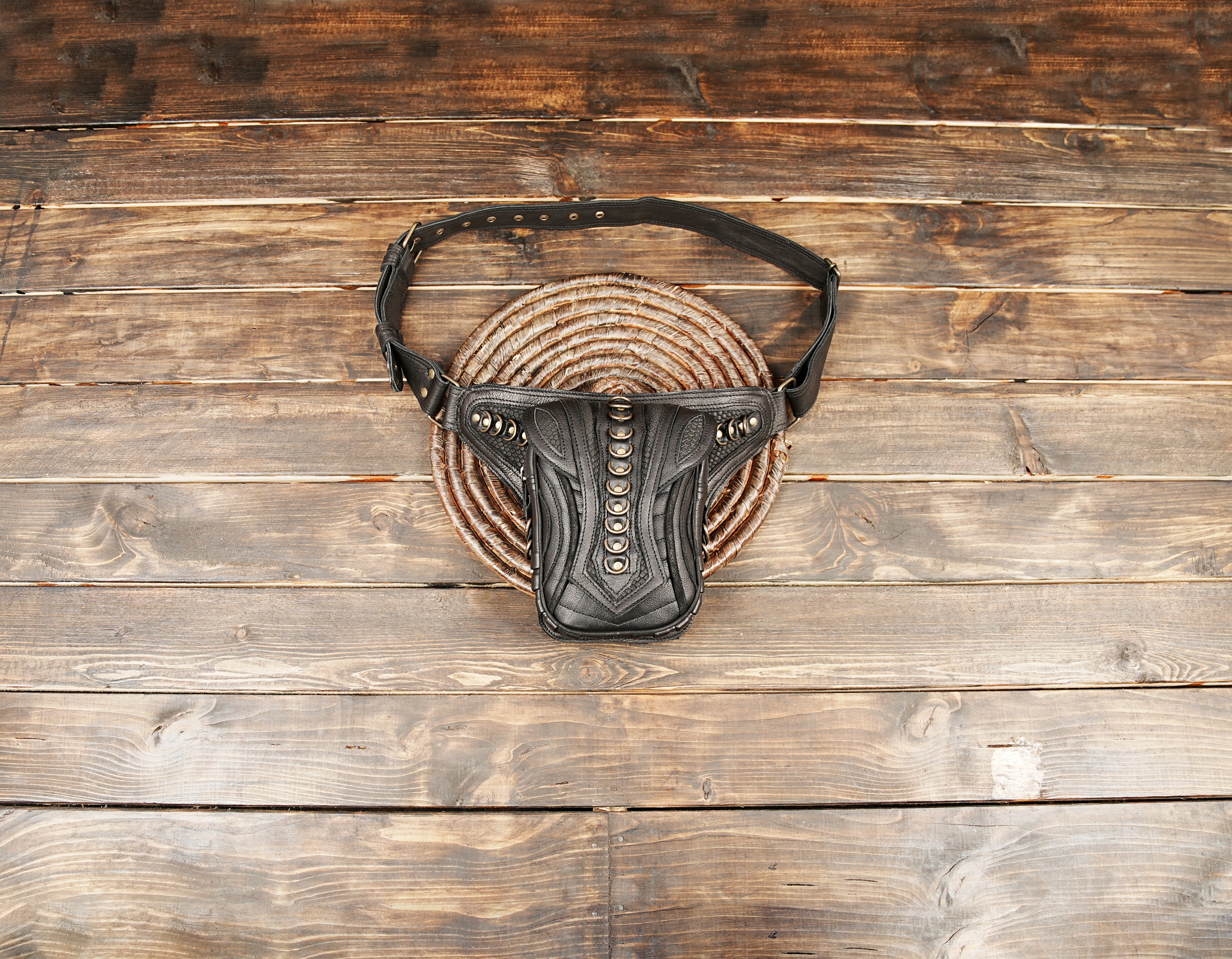 Black leather utility belt bag with rivet design on wooden background