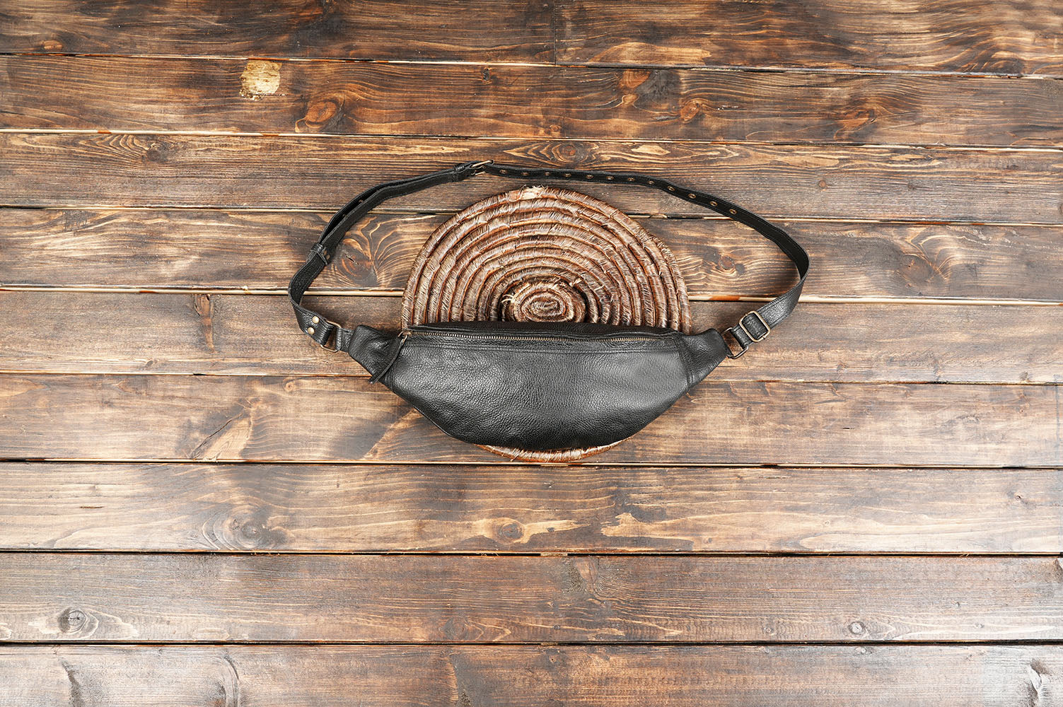 Handmade black leather waist bag with adjustable strap on wooden background