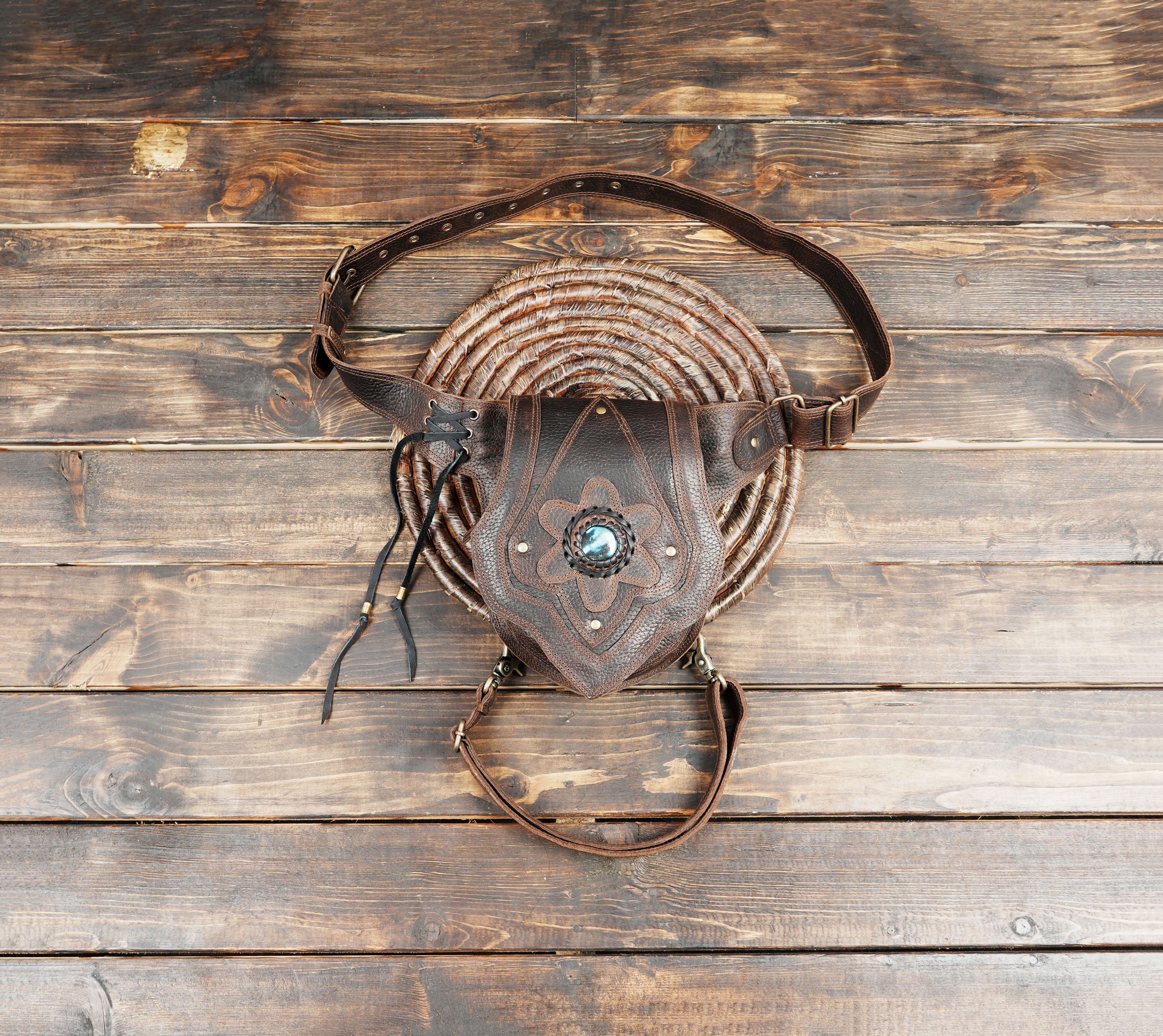 Brown leather hip bag with blue gemstone centerpiece on wooden background
