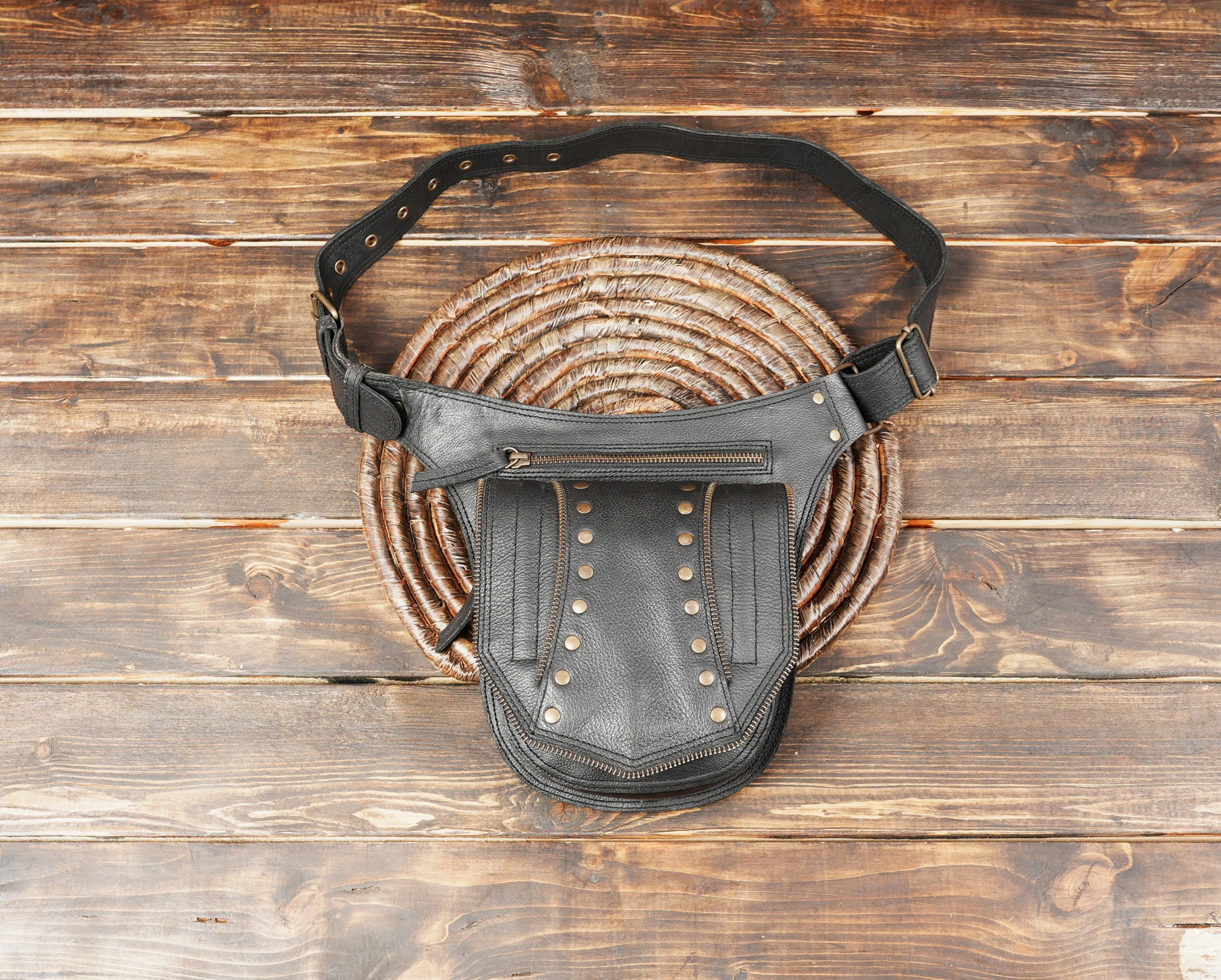 Close-up of black leather hip bag with brass studs and zippers