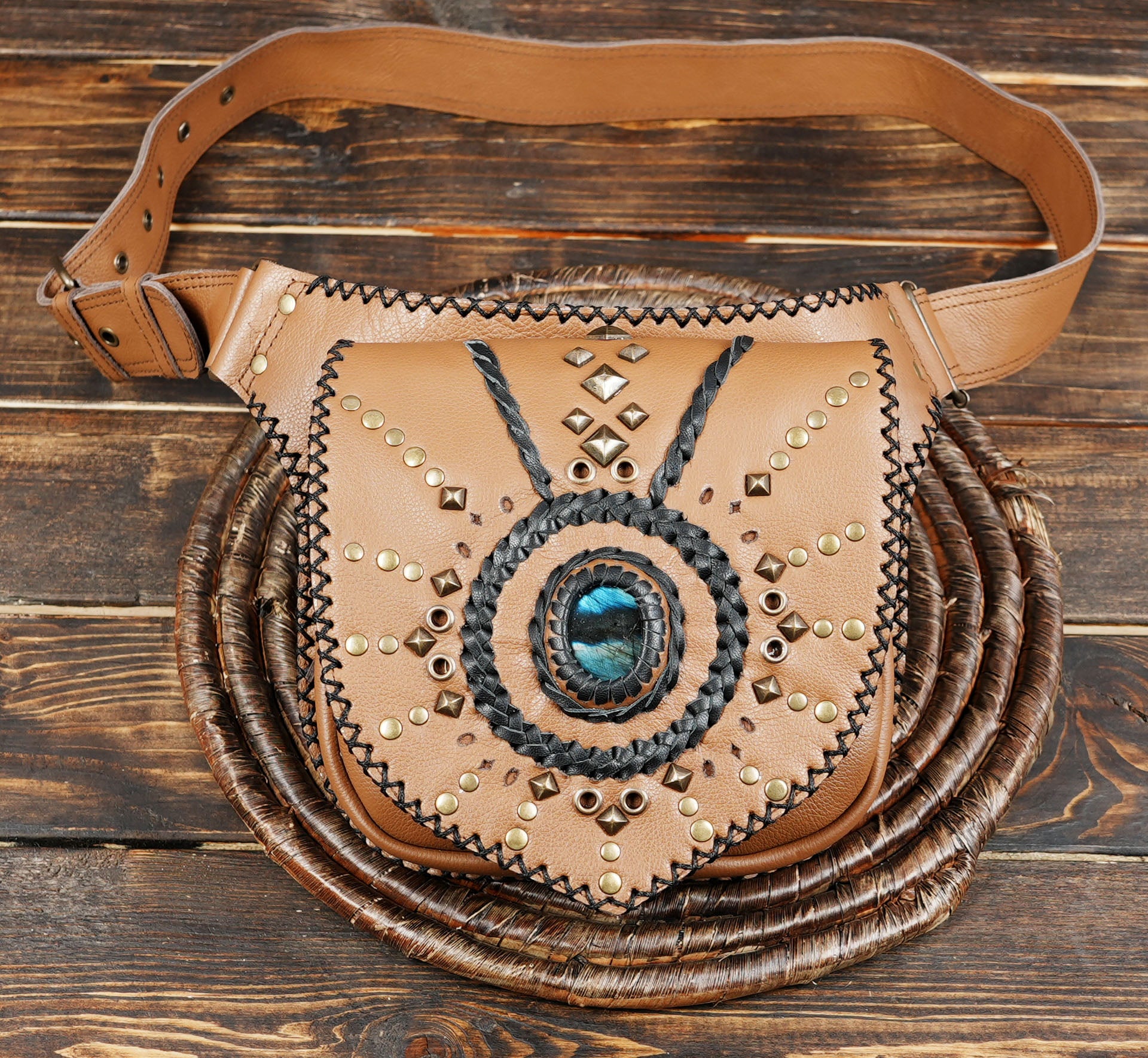 Close-up of tan leather hip pouch with black woven trim and brass studs