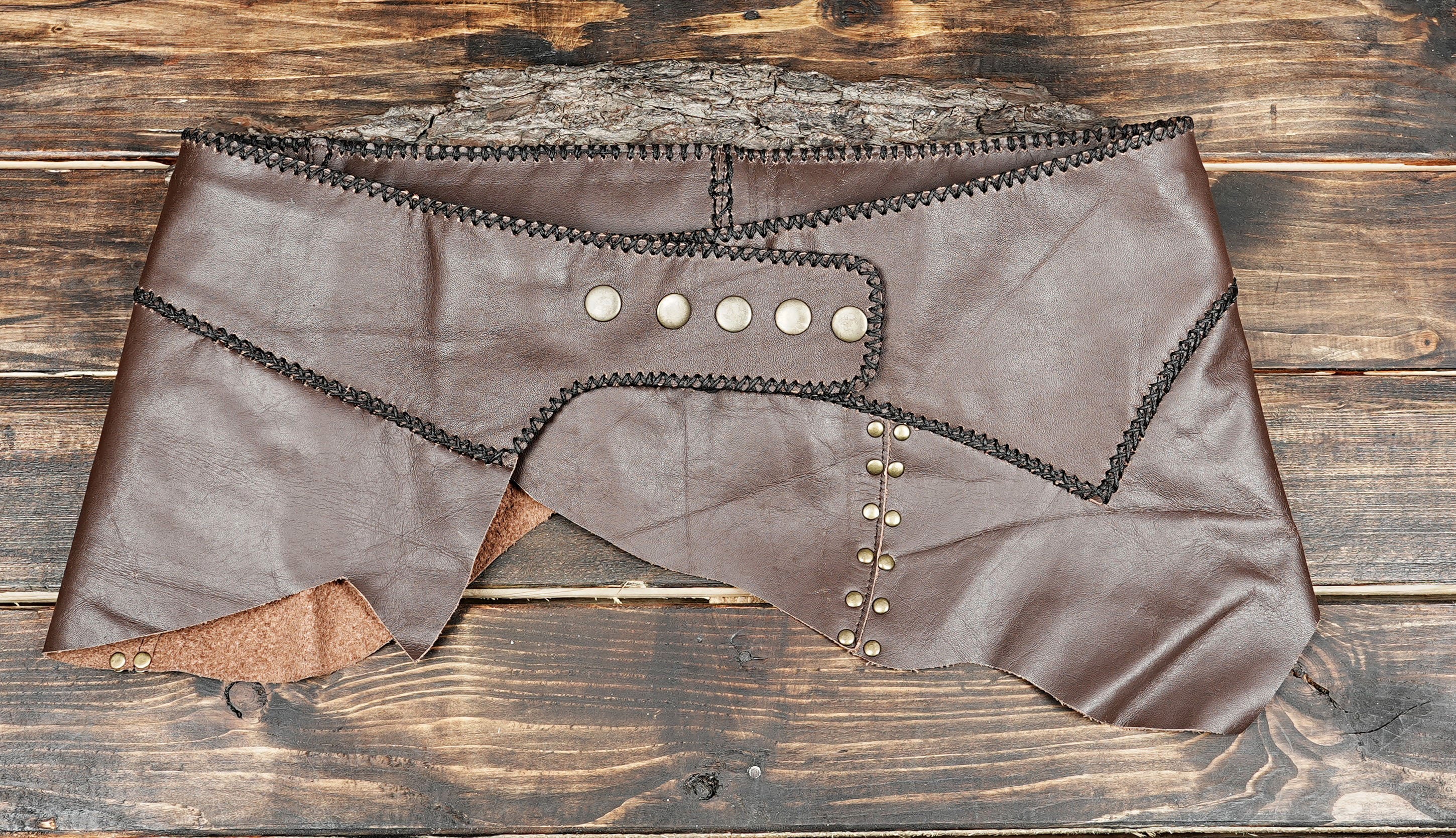 “Handmade brown leather skirt with brass studs and rustic cross-stitch trim, gothic steampunk festival wear.”