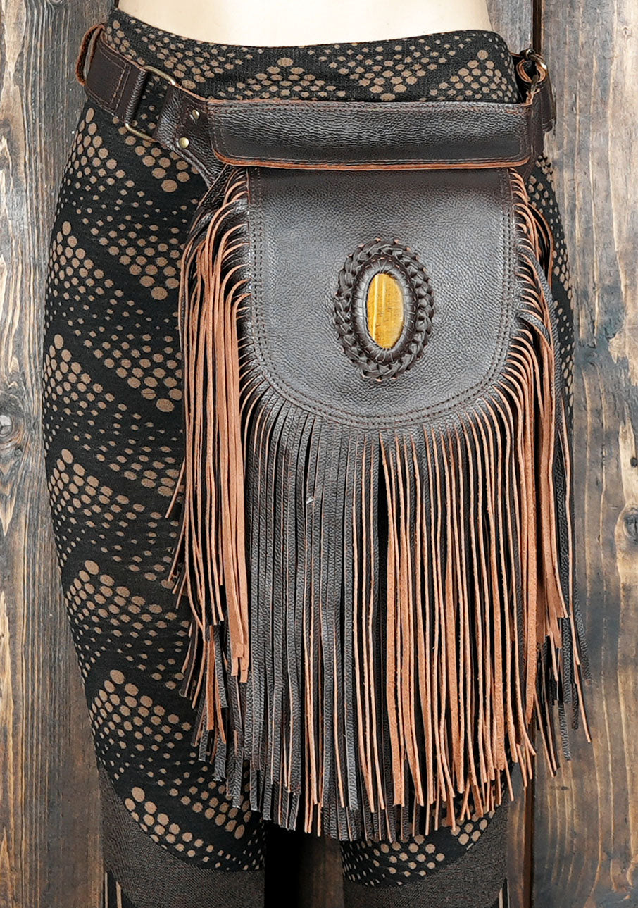 Brown and tan leather fringe belt bag with adjustable strap in front of gemstone 